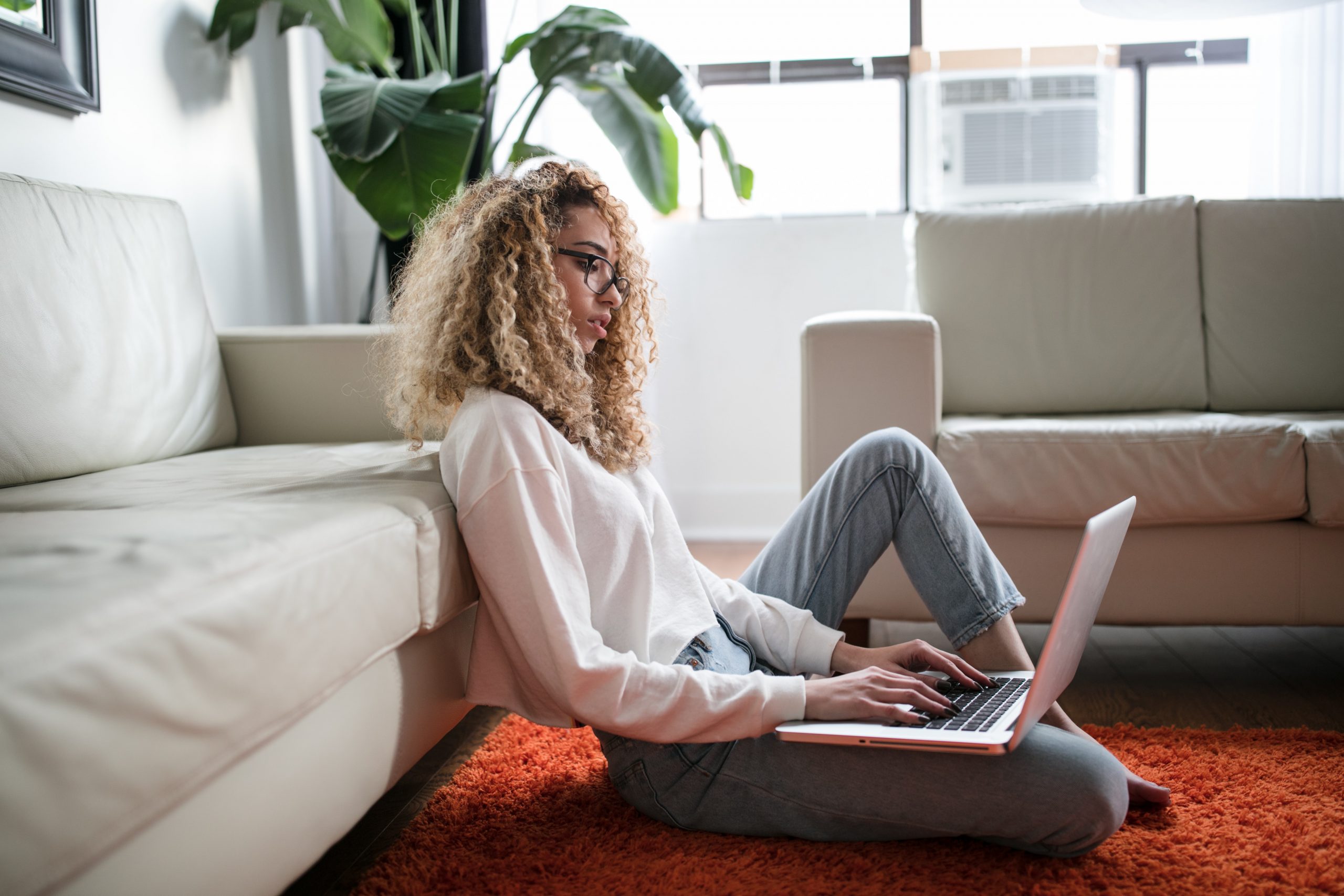 woman sitting on the floor in front of her couch using a laptop